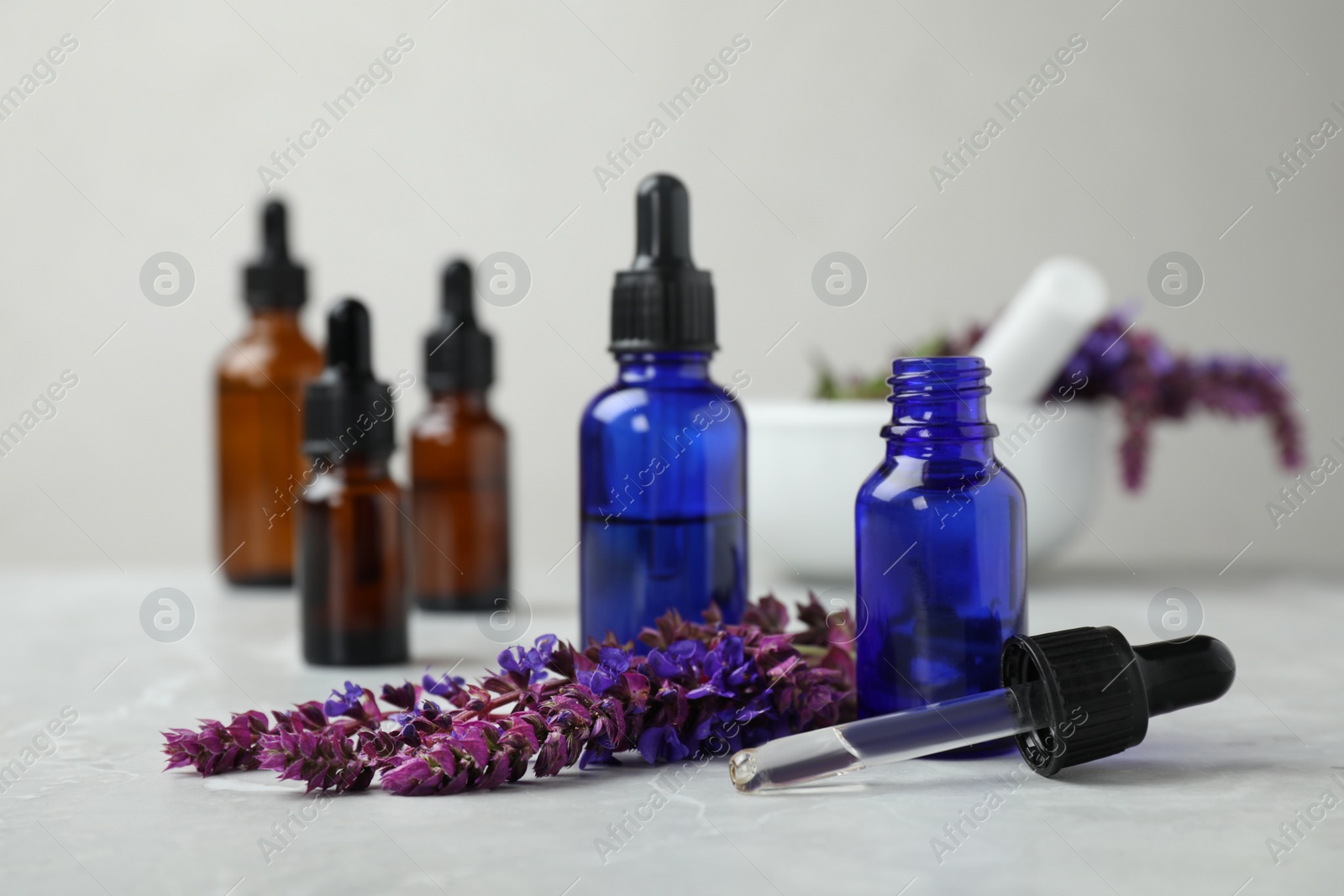 Photo of Bottles of sage essential oil and flowers on grey table