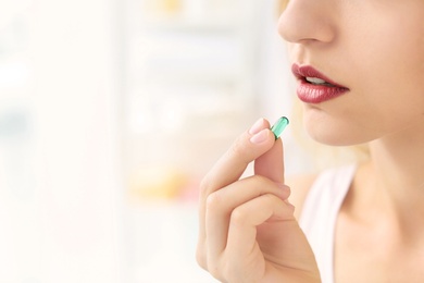 Photo of Young woman taking pill indoors