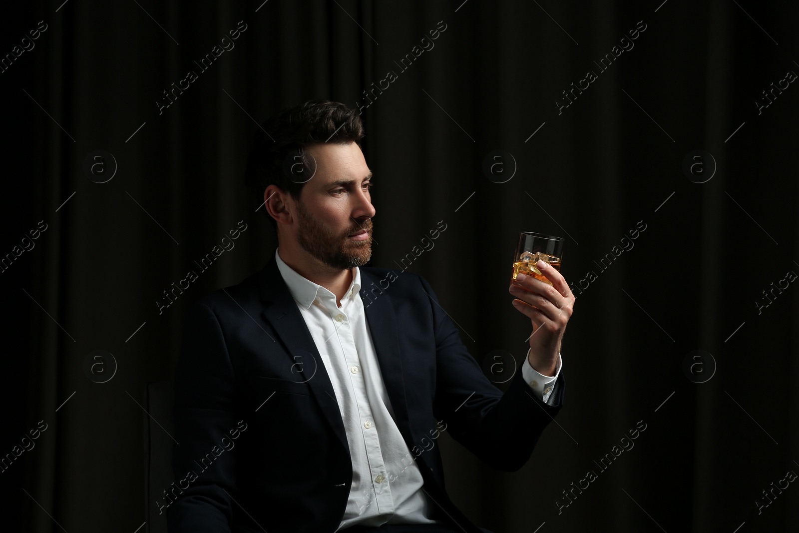 Photo of Handsome man in suit holding glass of whiskey on black background