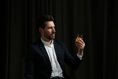 Photo of Handsome man in suit holding glass of whiskey on black background