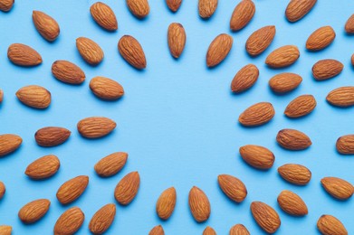 Photo of Delicious raw almonds on light blue background, flat lay. Space for text