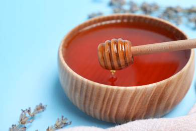 Wooden bowl with organic honey and dipper on light blue background, closeup