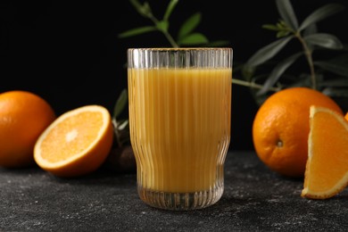 Photo of Tasty fresh oranges, juice and leaves on black table, closeup