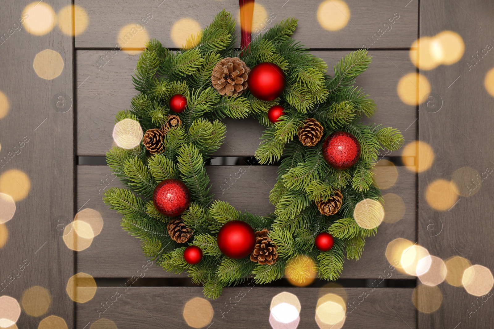 Photo of Christmas wreath with red baubles and cones hanging on wooden door