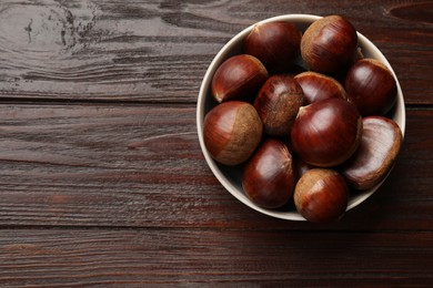 Photo of Sweet fresh edible chestnuts in bowl on wooden table, top view. Space for text