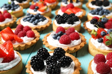 Photo of Many different berry tarts on blue wooden table. Delicious pastries