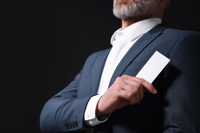 Photo of Businessman holding blank business card on black background, closeup. Space for text