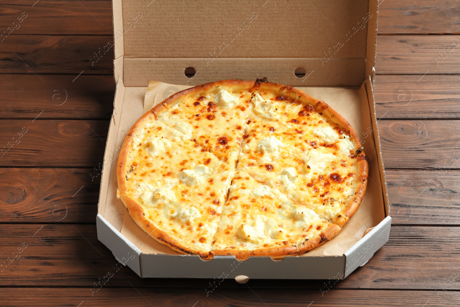 Photo of Carton box with delicious pizza on wooden background