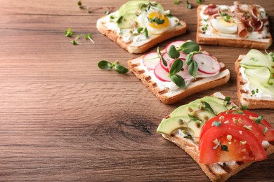 Different delicious sandwiches with microgreens on wooden table. Space for text