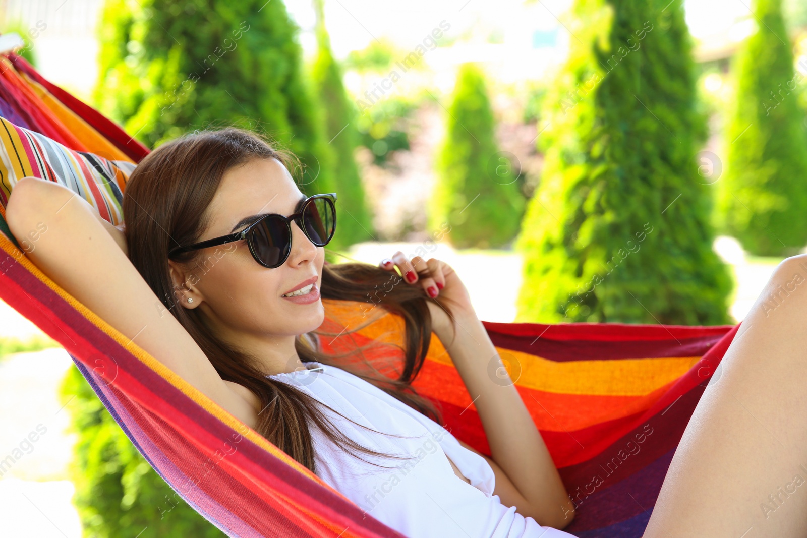 Photo of Young woman relaxing in hammock outdoors on warm summer day