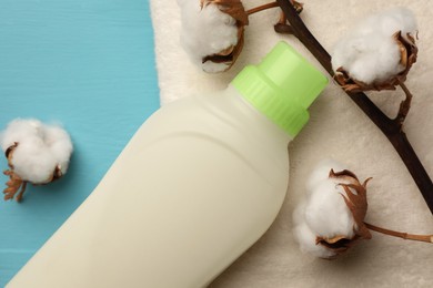 Photo of Bottle of fabric softener, terry towel and cotton flowers on light blue wooden table, flat lay
