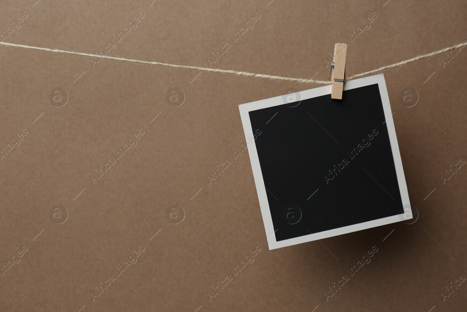 Photo of Wooden clothespin with empty instant frame on twine against brown background. Space for text