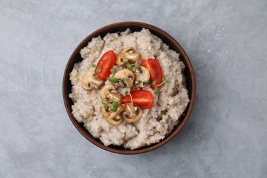 Photo of Delicious barley porridge with mushrooms, tomatoes and microgreens in bowl on gray table, top view