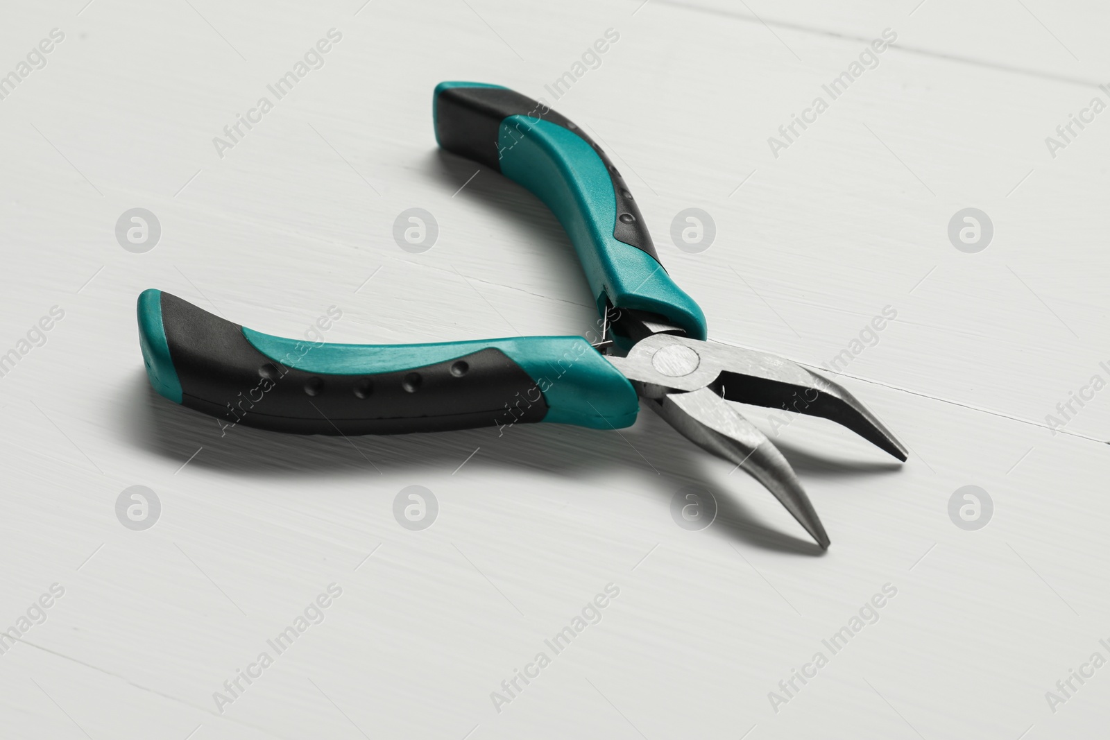 Photo of Bent nose pliers on white wooden table, closeup