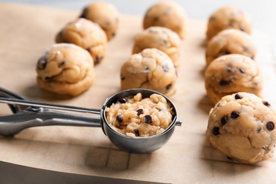 Photo of Raw cookie dough with chocolate chips and scoop on parchment paper, closeup