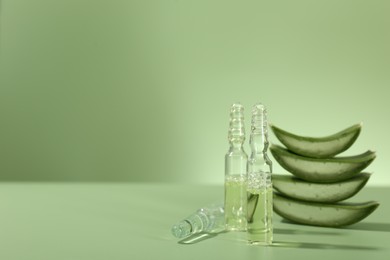 Photo of Skincare ampoules with extract of aloe vera and cut leaves on pale green background. Space for text
