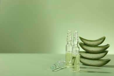 Skincare ampoules with extract of aloe vera and cut leaves on pale green background. Space for text