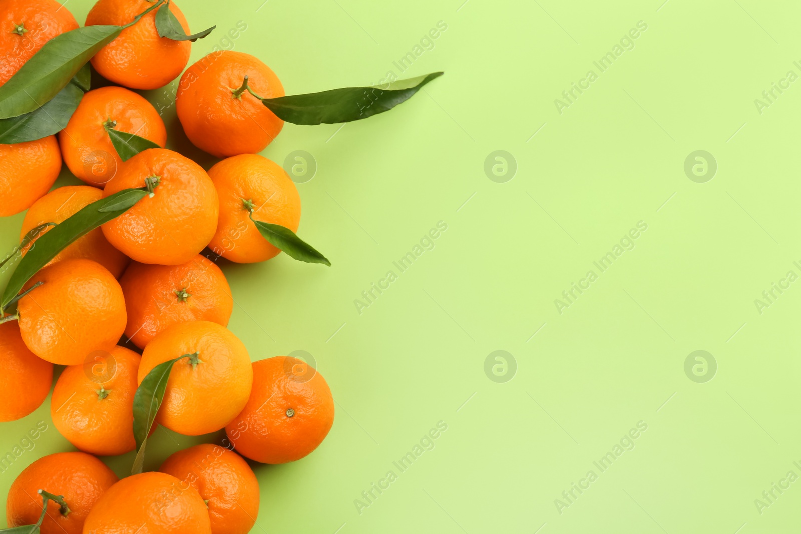 Photo of Fresh tangerines with green leaves on light green background, flat lay. Space for text