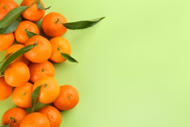 Fresh tangerines with green leaves on light green background, flat lay. Space for text