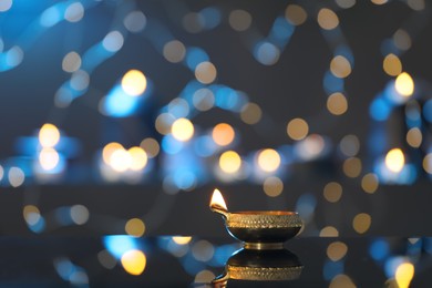 Photo of Lit diya on table against blurred lights, space for text. Diwali lamp