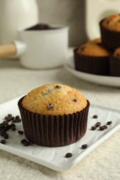 Delicious sweet muffin with chocolate chips on light textured table, closeup