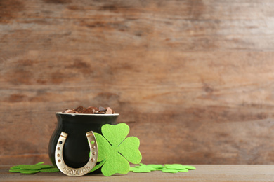 Photo of Pot of gold coins, horseshoe and clover leaves on wooden table, space for text. St. Patrick's Day celebration