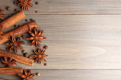Aromatic anise stars, pepper and cinnamon sticks on wooden table, flat lay. Space for text