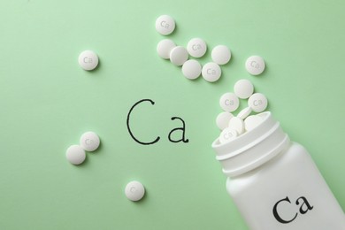 Photo of Flat lay composition with calcium supplement pills on light green background