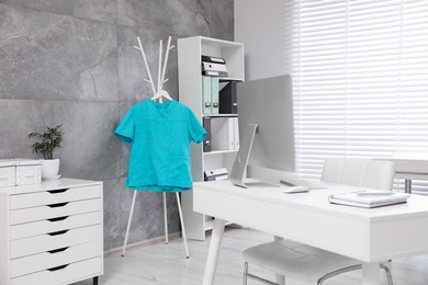 Photo of Turquoise medical uniform hanging on rack in clinic
