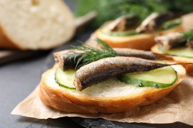 Photo of Delicious sandwich with sprats, cucumbers and dill on slate board, closeup