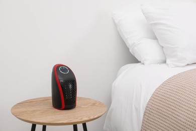 Photo of Modern compact electric heater on coffee table near bed indoors