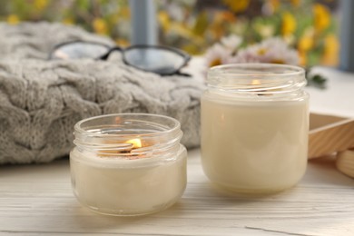 Photo of Burning scented candles, warm sweater, glasses and chamomile flowers on white wooden table near window