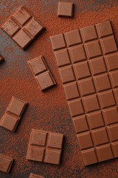 Pieces of tasty chocolate and cocoa powder on grey table, flat lay
