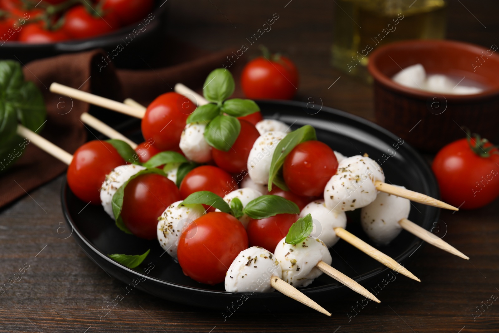 Photo of Delicious Caprese skewers with tomatoes, mozzarella balls, basil and spices on wooden table, closeup