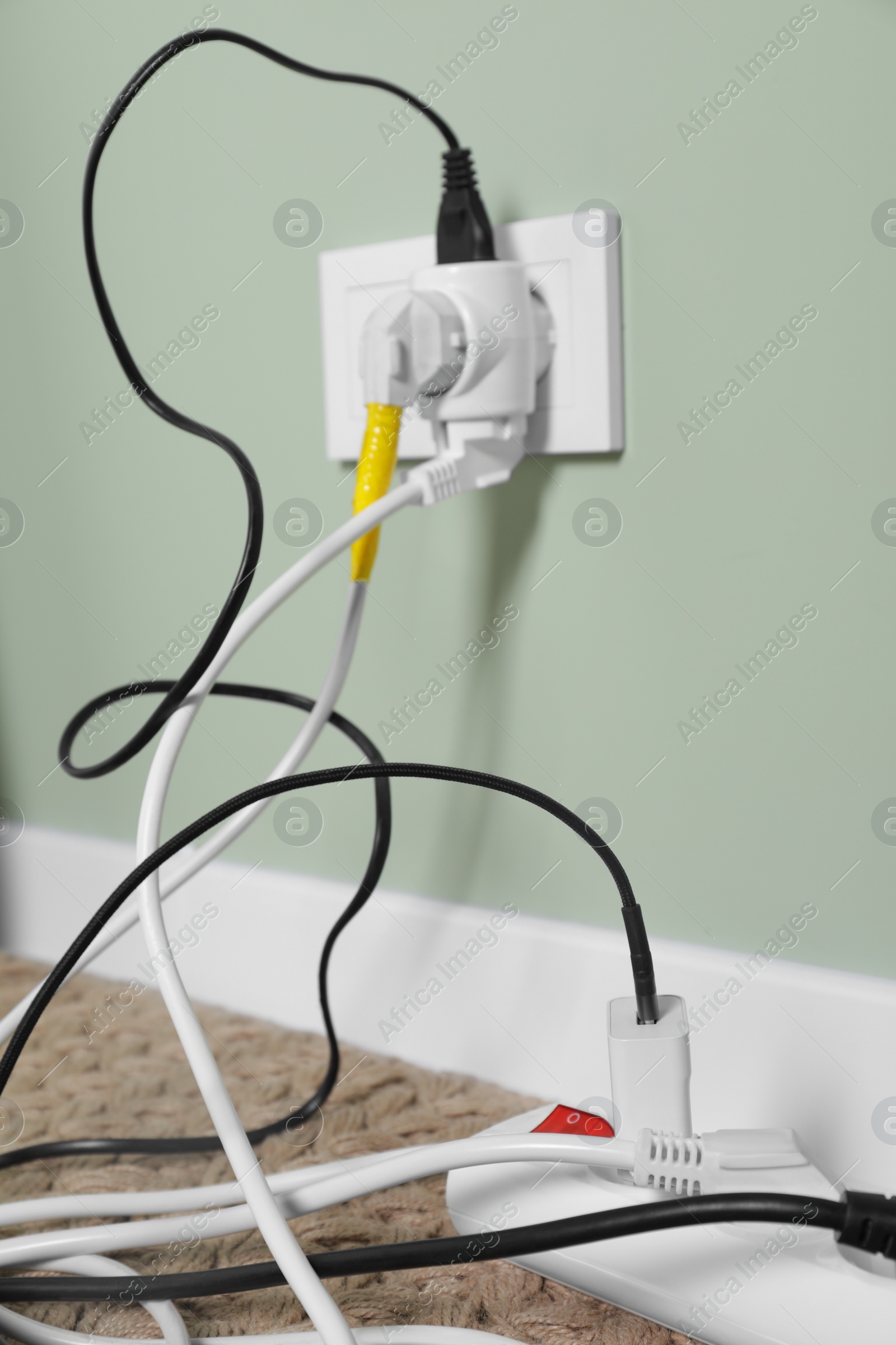 Photo of Different electrical plugs in socket and power strip on floor indoors, closeup