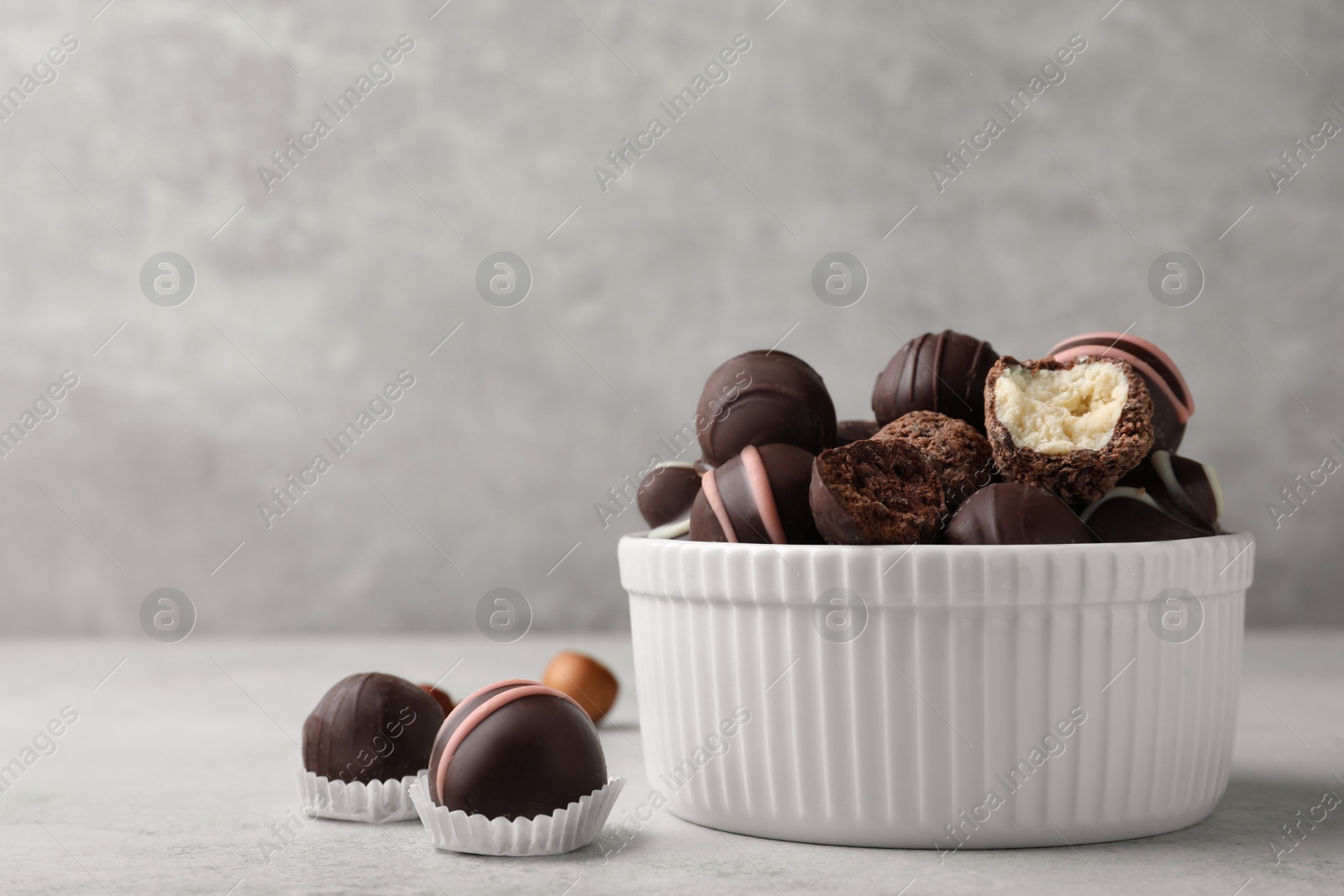 Photo of Different delicious chocolate truffles in bowl on light grey table. Space for text