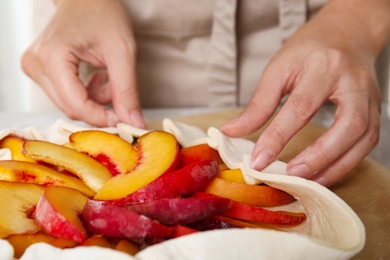 Woman making peach pie at table, closeup