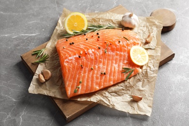 Photo of Wooden board with raw salmon and ingredients for marinade on grey background