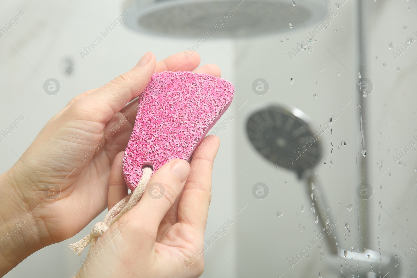 Photo of Woman holding pink pumice stone near shower stall in bathroom, closeup. Space for text