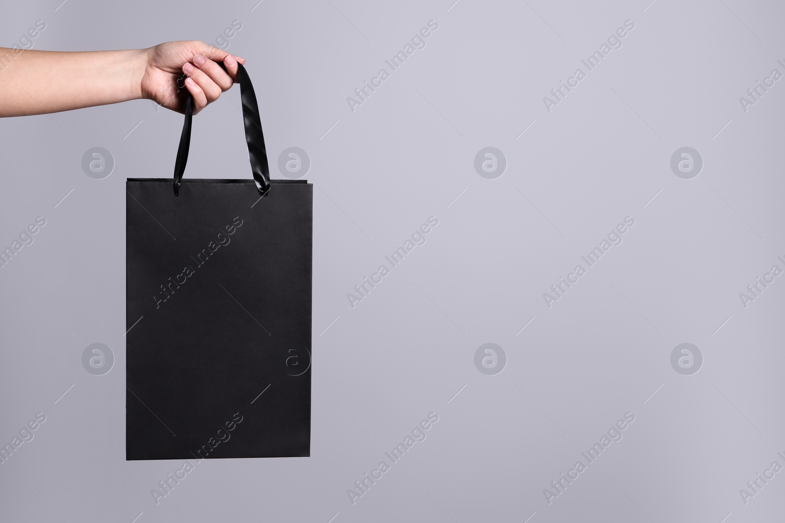 Photo of Woman holding paper shopping bag on grey background, closeup. Space for text