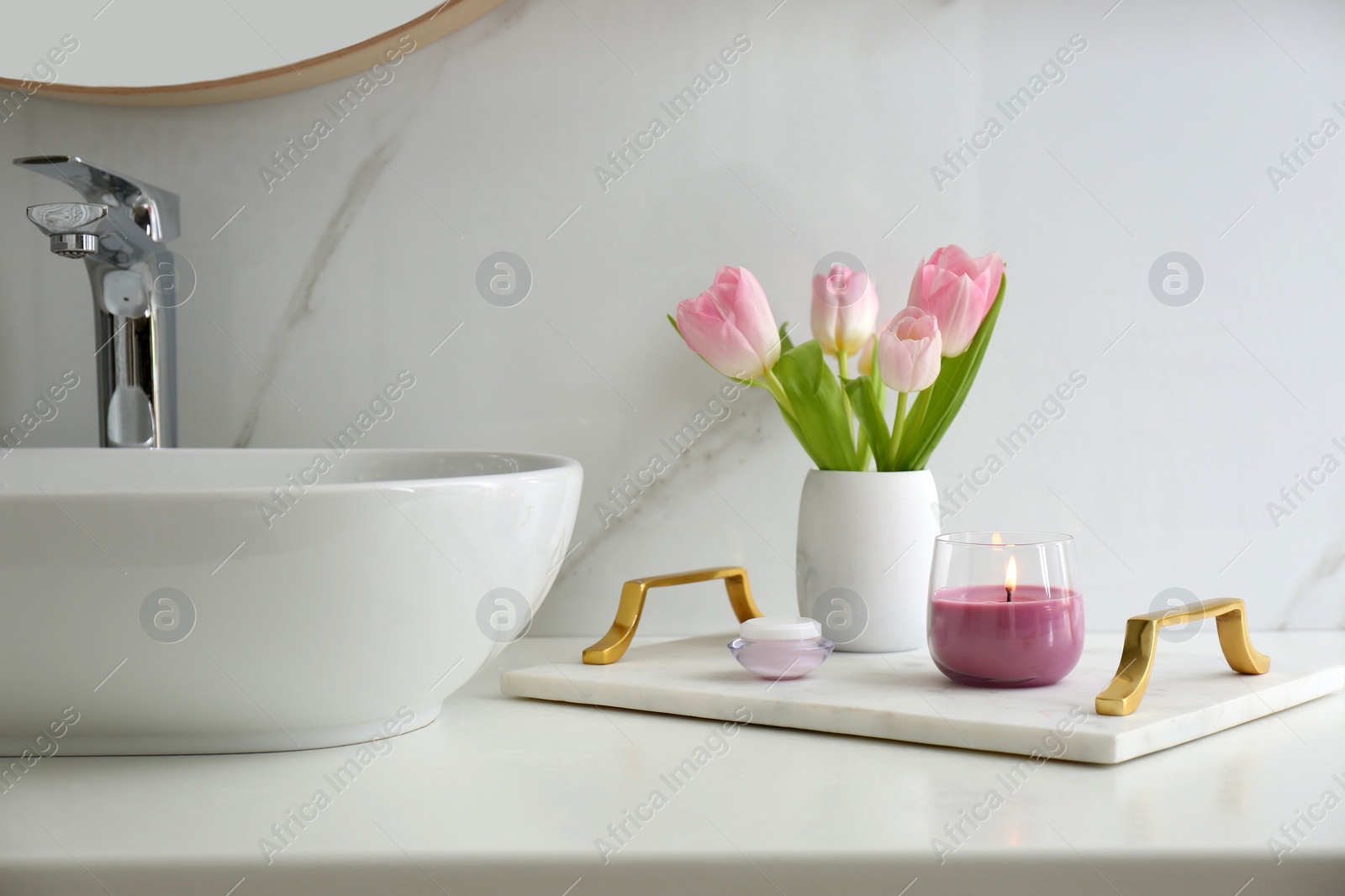 Photo of Beautiful flowers and candle on countertop in bathroom. Interior decor