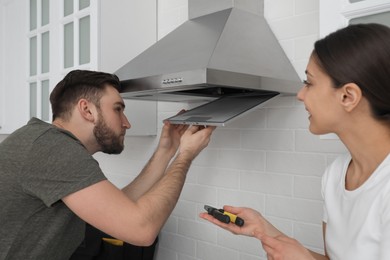 Photo of Man repairing modern cooker hood and woman in kitchen