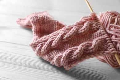 Soft pink yarn, knitting and needle on white wooden table, closeup