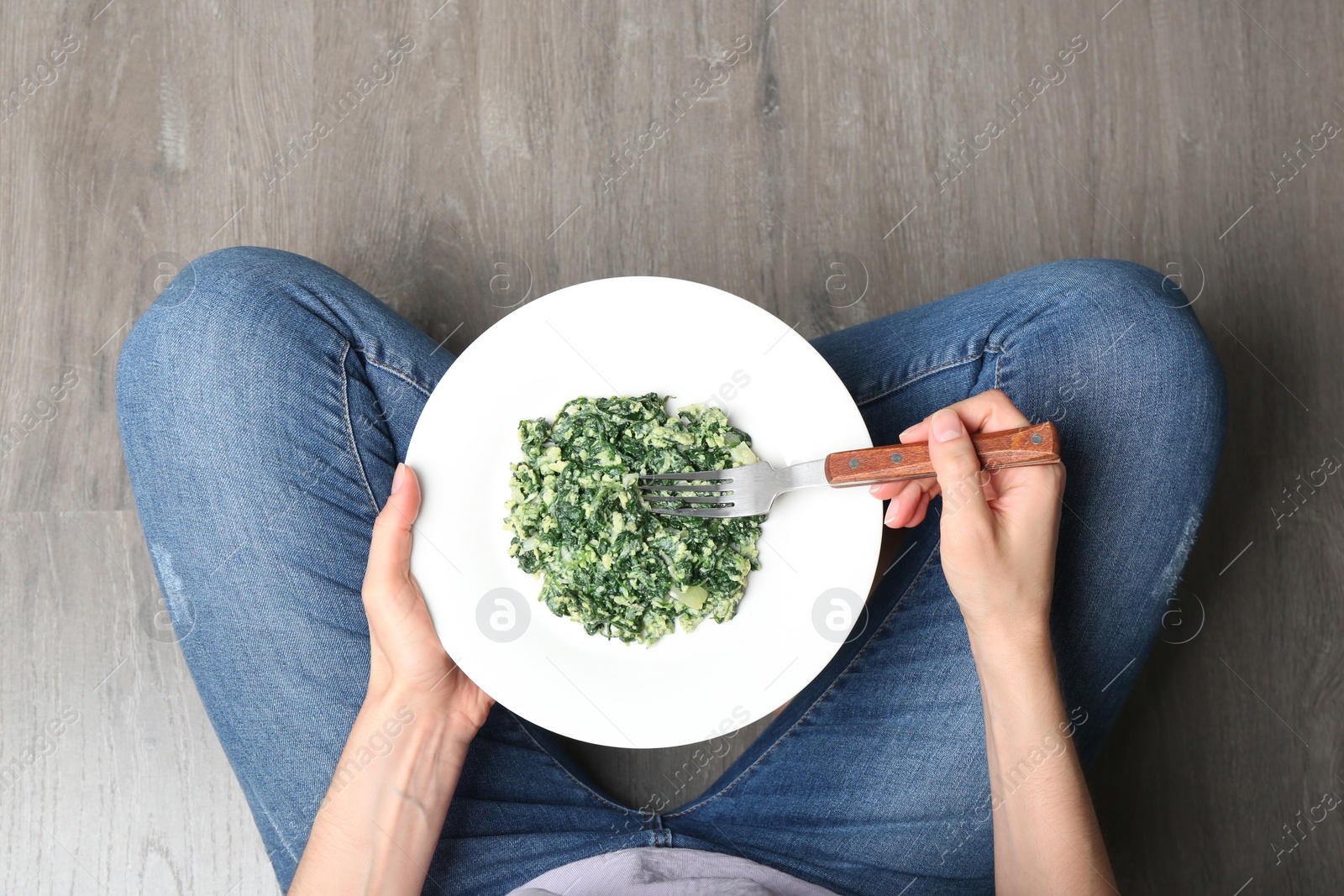 Photo of Young woman with tasty cooked spinach on wooden floor, top view. Healthy food