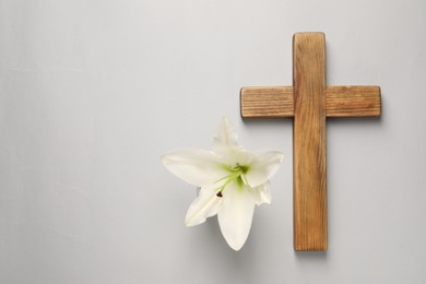 Photo of Wooden cross and lily flower on grey background, top view with space for text. Easter attributes