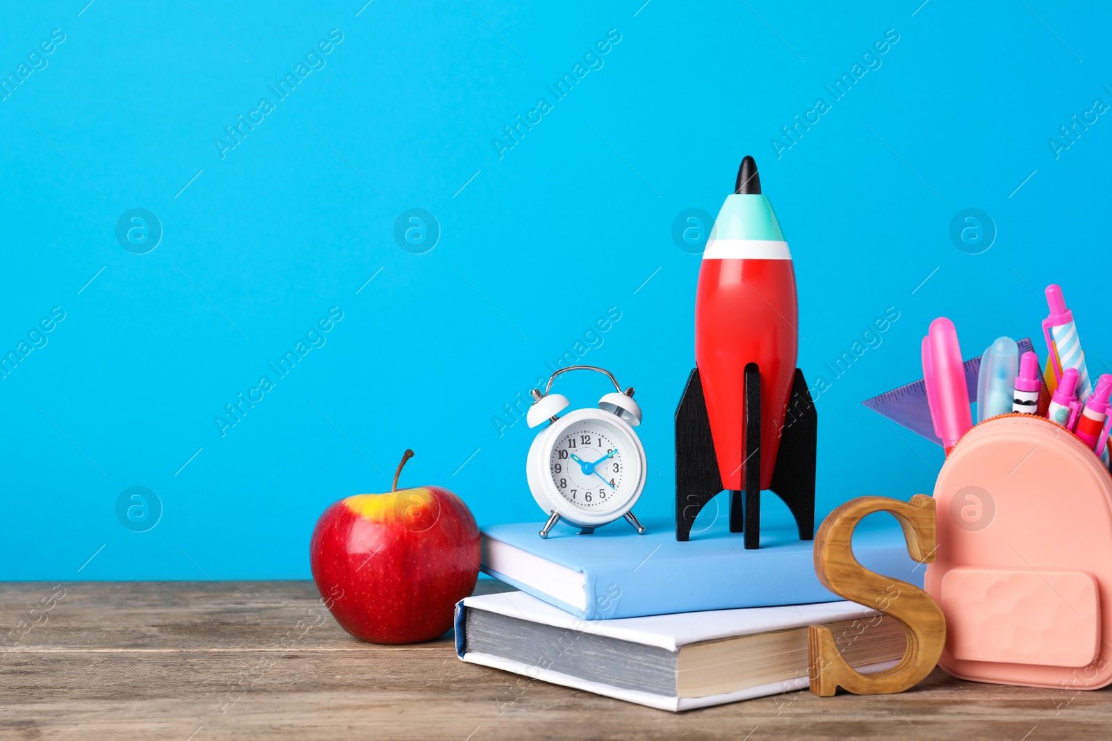 Photo of Bright toy rocket and school supplies on wooden desk. Space for text