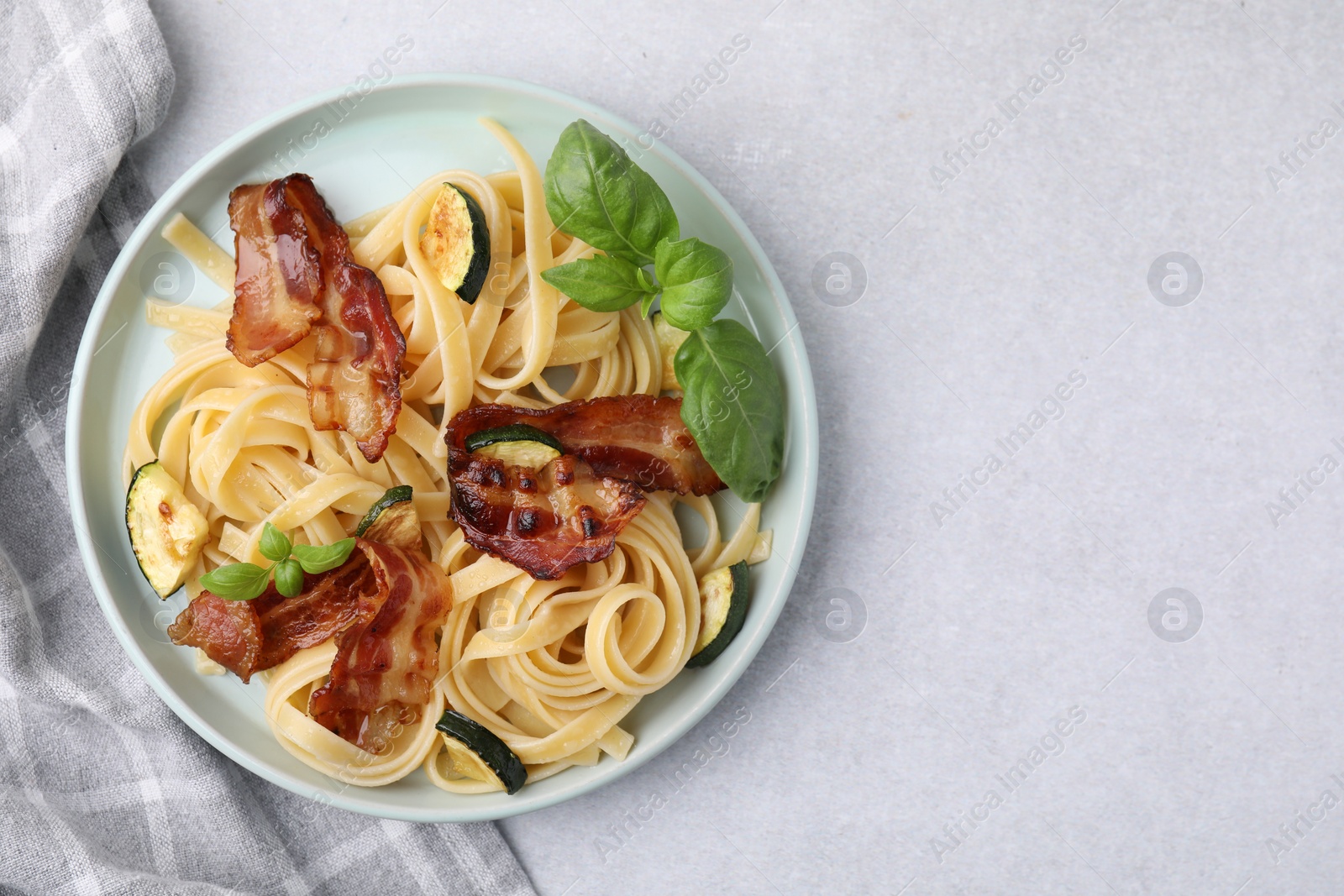 Photo of Tasty pasta with bacon and basil on light grey table, top view. Space for text