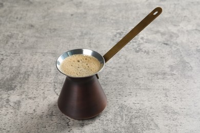 Photo of Turkish coffee pot with hot drink on grey table, space for text