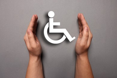 Image of Disability inclusion. Woman protecting wheelchair symbol on grey background, closeup