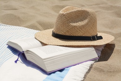 Photo of Beach towel with open book and straw hat on sand